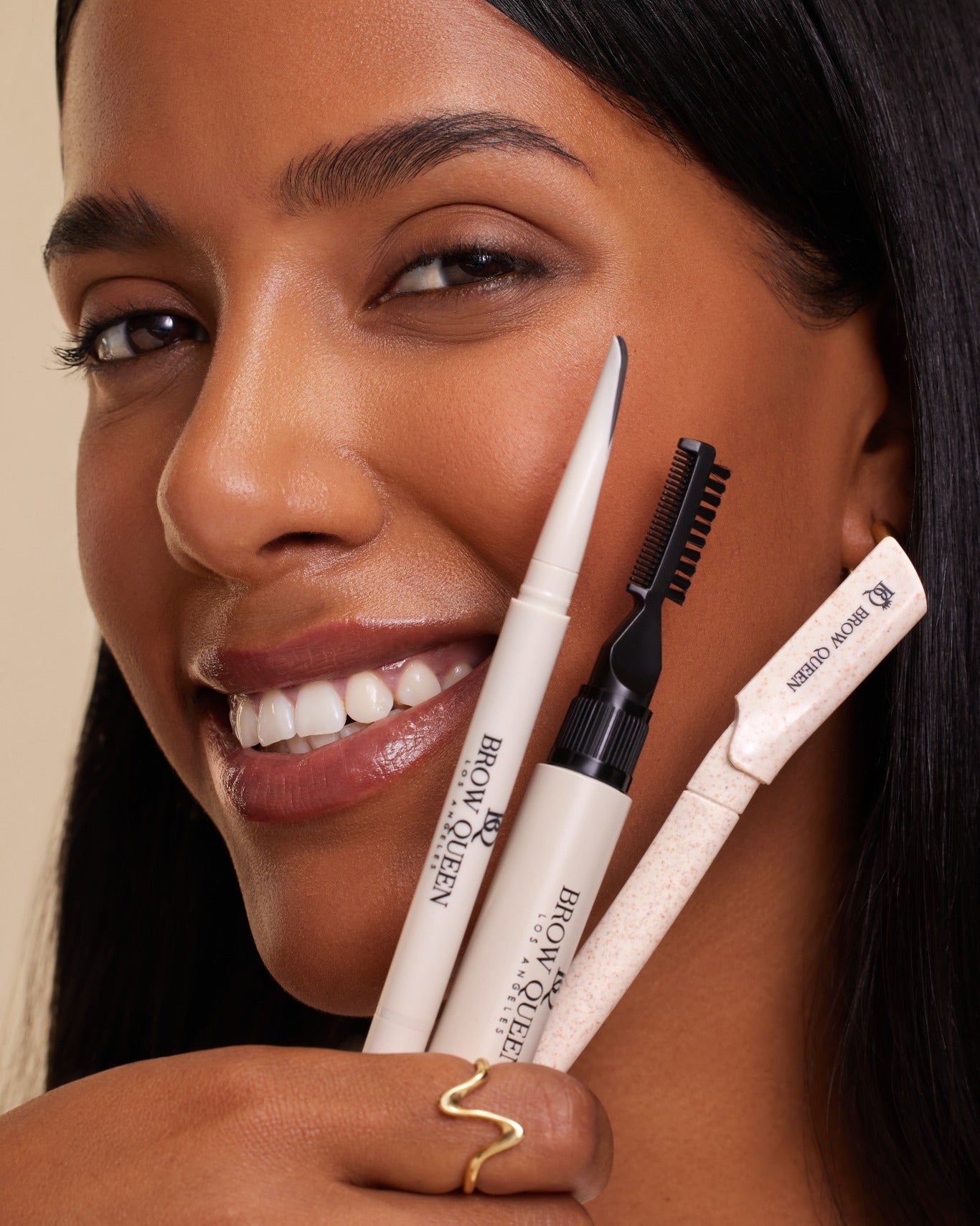 Woman holding brow grooming tools with a neutral background