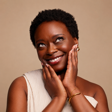 Woman with short hair smiling and touching her face against a beige background
