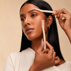 Woman using a brow brush on her face with a beige background