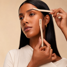 Woman using a brow brush on her face with a beige background