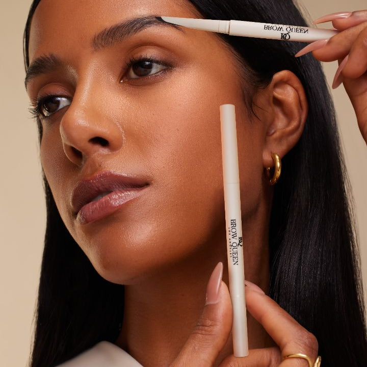Woman applying Brow Queen eyebrow pencil to her eyebrows with a neutral background