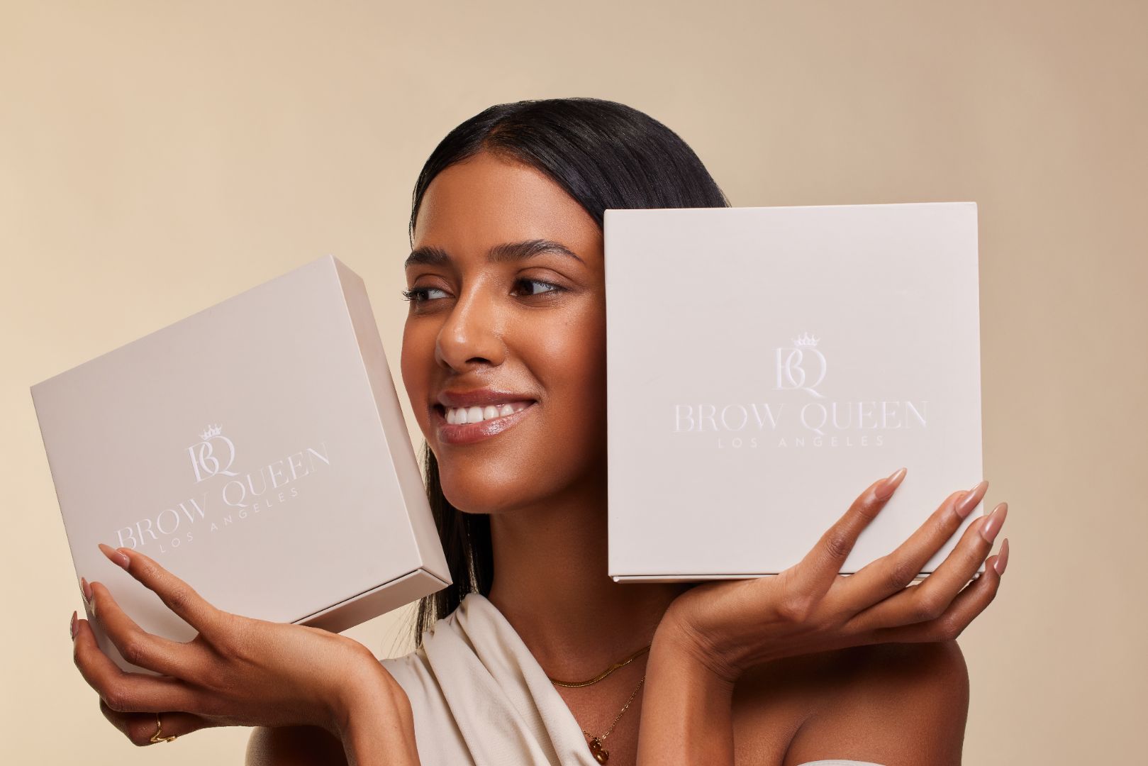 Woman holding two 'Brown Queen' boxes against a beige background