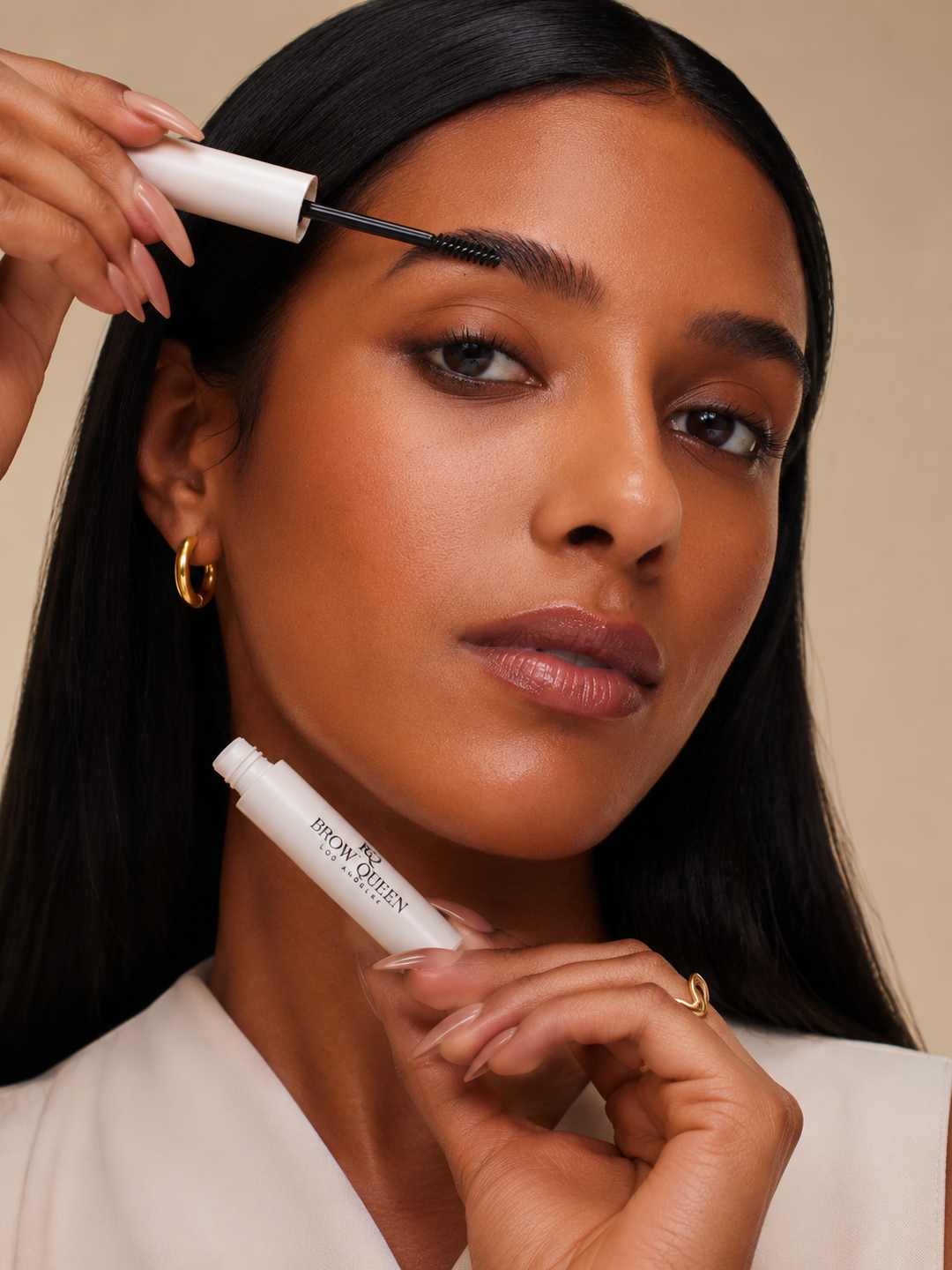 Woman applying brow gel with a brush against a neutral background