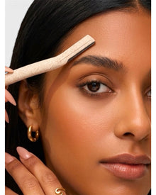 Close-up of a woman using the dermaplaning tool on her eyebrow for precise shaping.