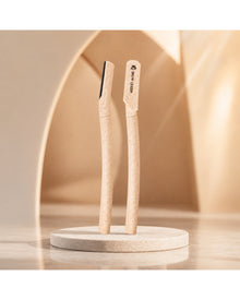 Two dermaplaning tools standing upright on a round stand against a warm neutral background.